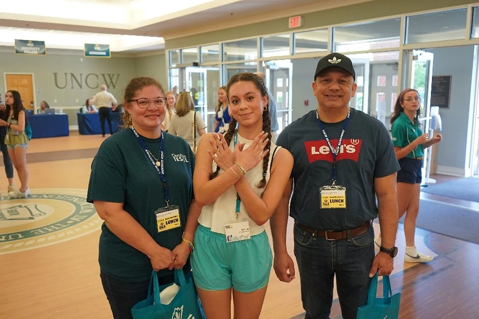 A UNCW student posing with  her parents making the wings up sign with her hands at orientation.